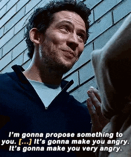 a man is talking to another man in front of a brick wall while wearing a hoodie .