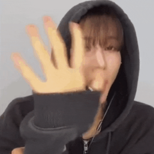 a woman in a hoodie is making a funny face with her hand .