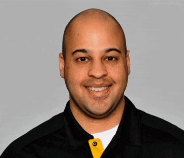 a man wearing a black shirt with a yellow button on the collar smiles