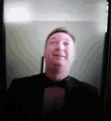 a man in a tuxedo and bow tie is smiling in a video call .
