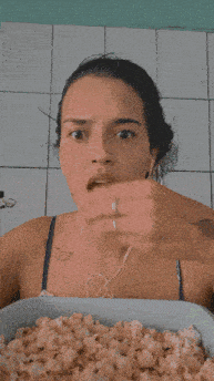 a woman with a tattoo on her arm is holding a bowl of popcorn and making a funny face