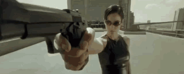 a woman is pointing a gun at someone while wearing sunglasses .