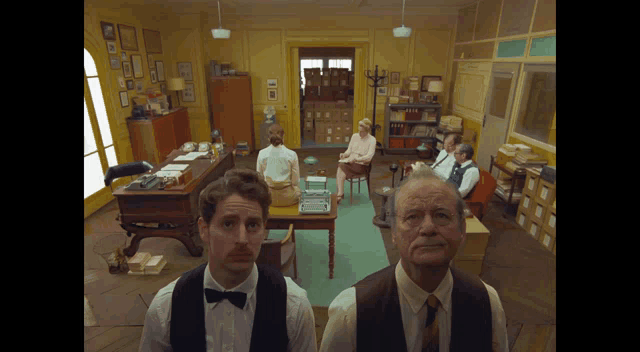 a man in a bow tie stands in front of a group of people