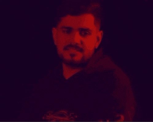 a man with a beard wearing a black hoodie is smiling with his arms crossed .