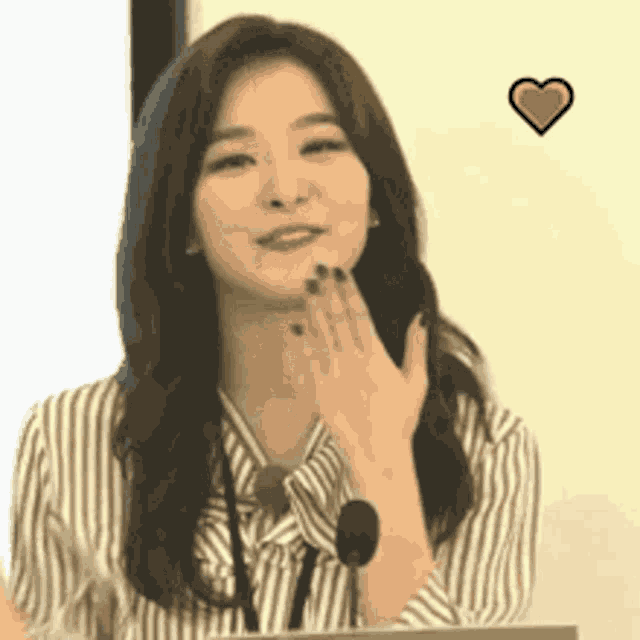 a woman in a striped shirt is blowing a kiss with a heart above her .