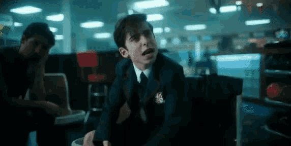 a young man in a suit and tie is sitting in a bowling alley with his mouth open .