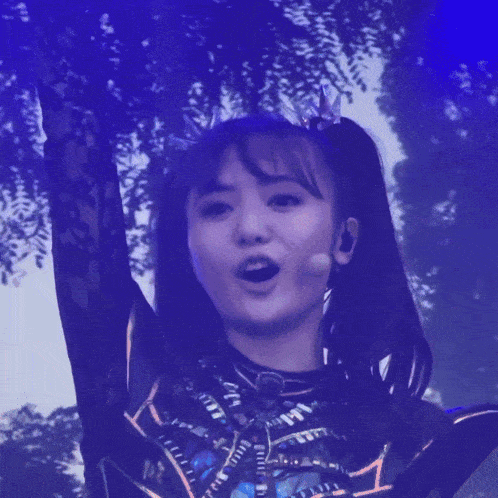a girl with a crown on her head is singing into a microphone with her arms in the air