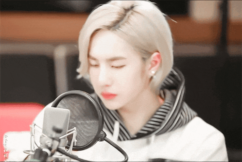 a man with blonde hair is sitting in front of a microphone with his eyes closed