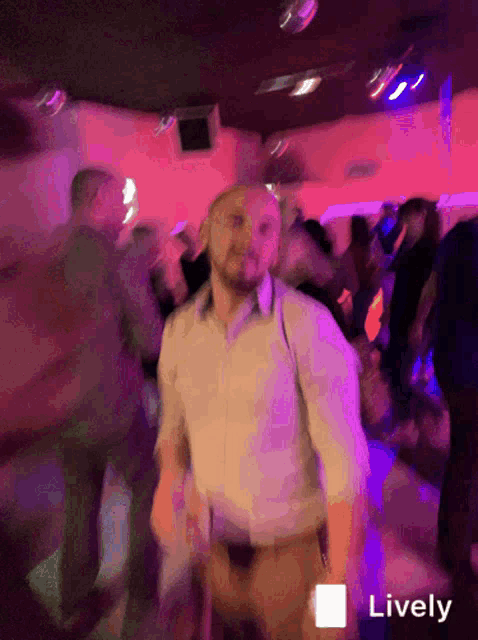 a man in a white shirt is dancing in a crowded room with purple lights and the word lively in the corner