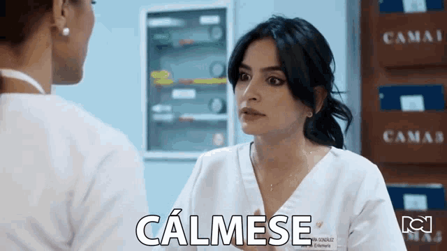 a woman in a white scrub is talking to another woman and the word calmese is written on the screen
