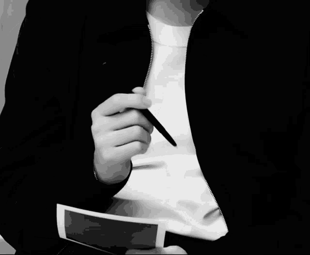 a man in a black jacket holds a pen and a piece of paper