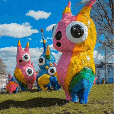 a group of colorful sculptures in a field with trees in the background