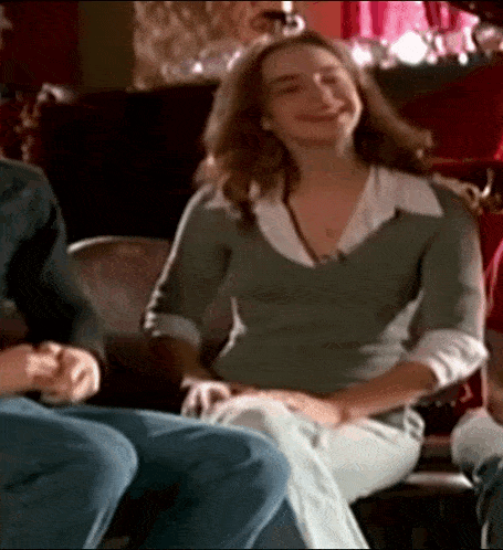a woman in a green sweater sits on a couch laughing
