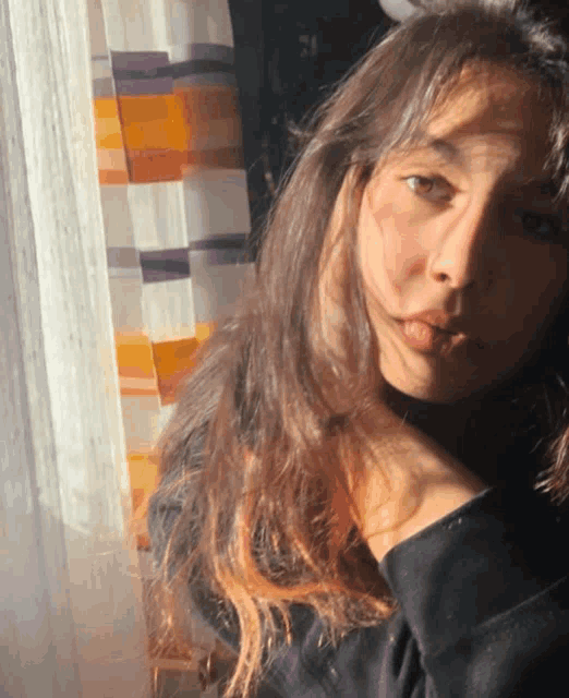 a woman 's face is visible in front of a window with a striped curtain