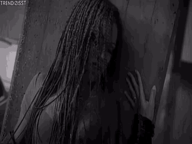 a black and white photo of a woman standing in the rain behind a glass door .