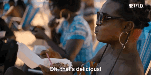 a woman is sitting in a beach chair eating food from a styrofoam container and says oh that 's delicious