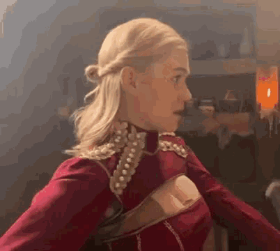 a woman with blonde hair is wearing a red top and pearls