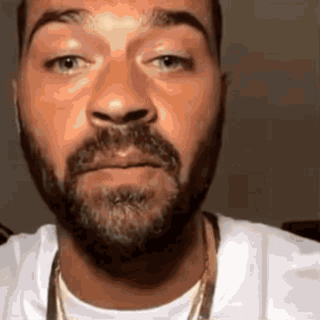 a man with a beard is wearing a white shirt and gold chain .