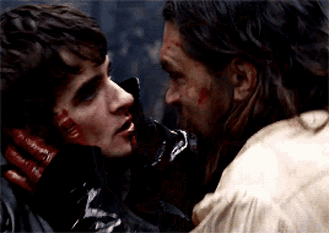 a man with blood on his face is holding another man 's neck