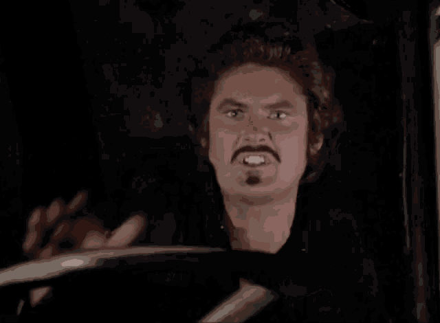 a man with a mustache is making a funny face while looking out of a car window .