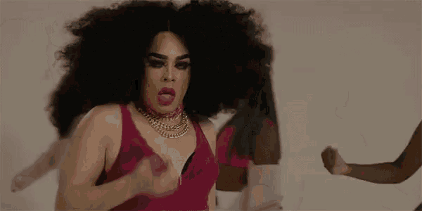 a drag queen is sticking out her tongue while wearing a pink bra .
