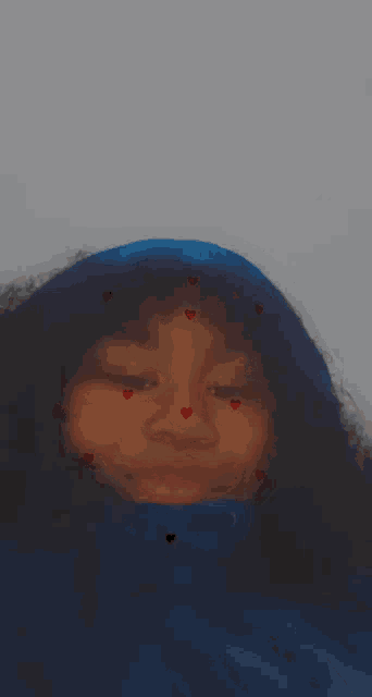 a young girl with curly hair is wearing a blue hoodie and hearts on her face .