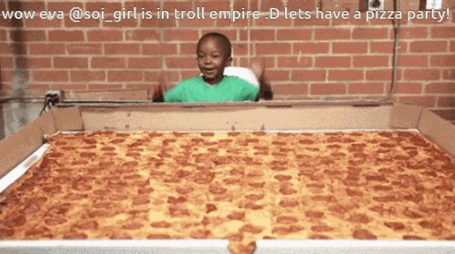 a boy in a green shirt is sitting in a box with a giant pizza in it