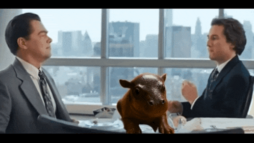 two men are sitting at a table with a pig sitting on it