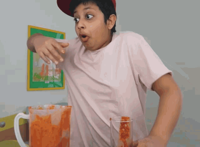 a boy in a pink shirt is standing next to a pitcher of tomato juice