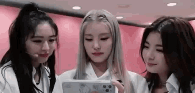 three young women are looking at a cell phone together .