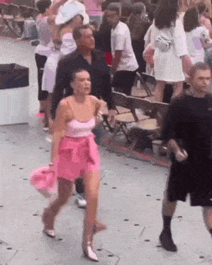 a woman in a pink dress is walking in front of a crowd of people