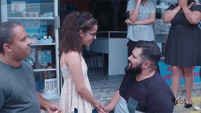 a man is kneeling down in front of a little girl and holding her hands .