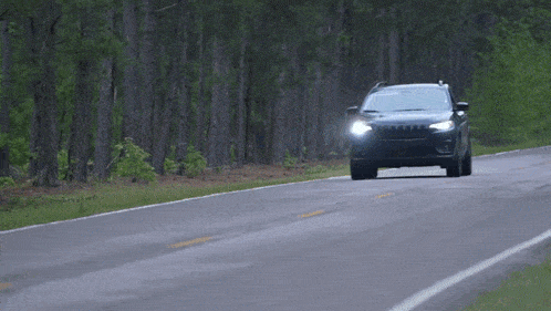 a black jeep is driving down a country road