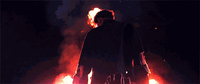 a man in a black jacket is standing in front of a fire in the dark