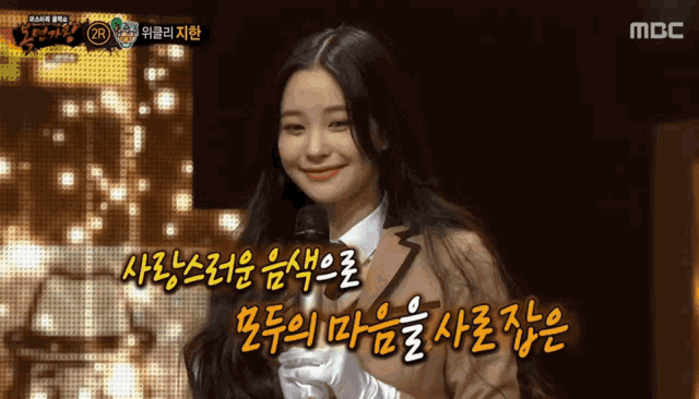 a woman in a suit and white gloves is smiling in front of a screen that says mbc