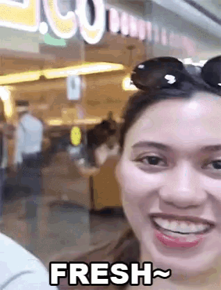 a woman wearing sunglasses is smiling in front of a sign that says " fresh "