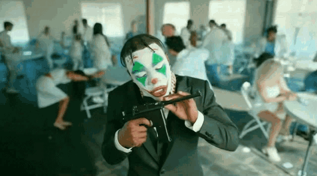 a man in a suit and clown mask is holding a gun in a room .