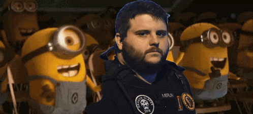 a man with a beard wearing a vest that says meun stands in front of a bunch of minions