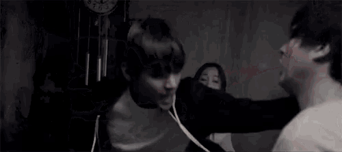 a person with blood on their shirt is being helped by another person in a dark room .