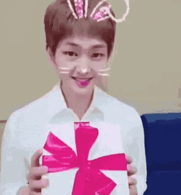 a young man wearing bunny ears is holding a white box with a pink bow .