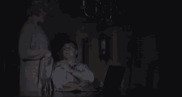 a man is sitting at a table with a laptop and a woman is standing next to him