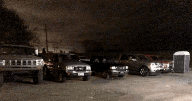 a row of trucks are parked in a parking lot with a purple portable toilet in the background