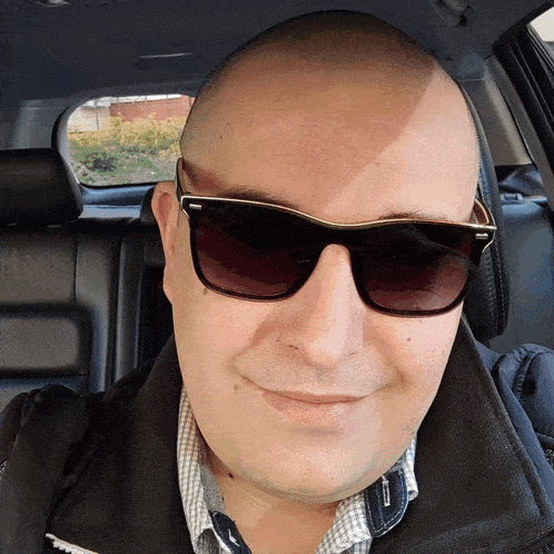 a man wearing sunglasses and a plaid shirt smiles in a car