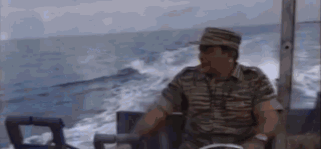 a man in a military uniform is driving a boat on the ocean .