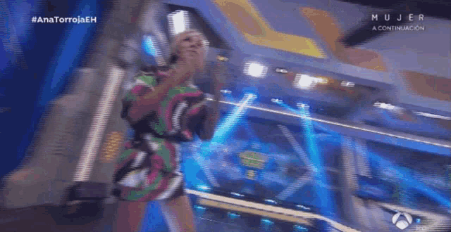 a woman in a colorful dress is dancing on a stage in front of a screen that says mujer
