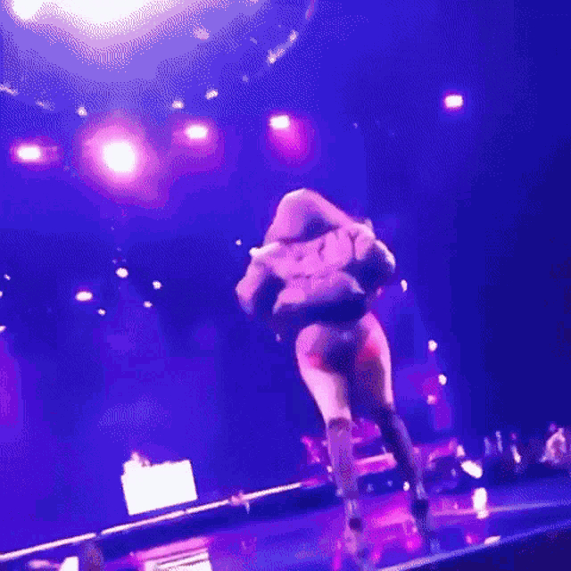 a woman is dancing on a stage with purple lights in the background .
