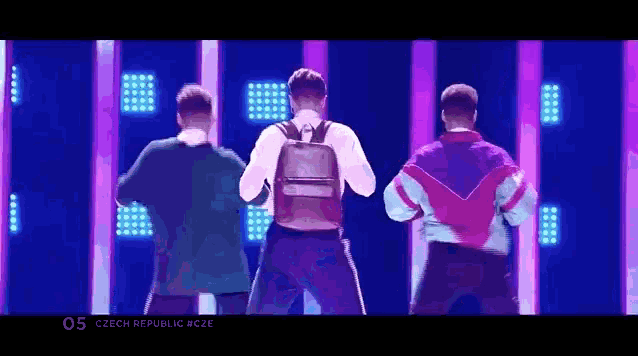 three men are dancing on a stage in front of a purple background .