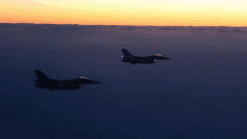 two fighter jets flying in the air at sunset