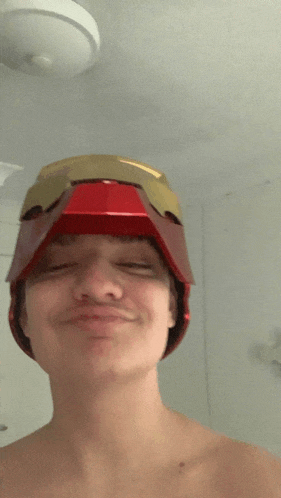 a shirtless young man wearing a red and gold helmet on his head