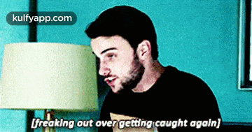 a man with a beard is sitting in front of a lamp and says freaking out over getting caught again